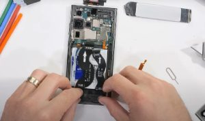 Hands lifting the battery out of an opened Samsung, replacement battery waiting alongside