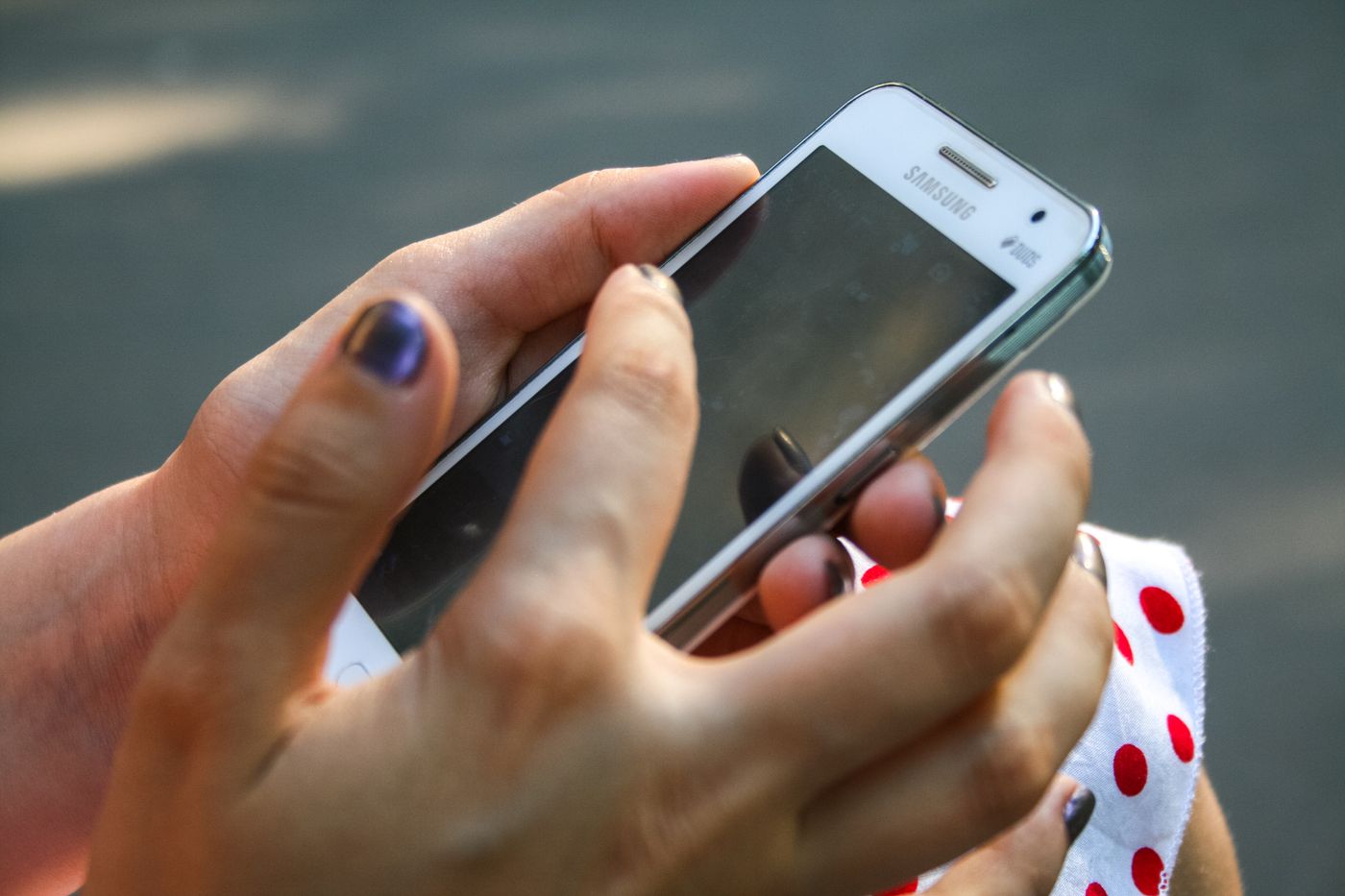 Fingertip resting on the dark touchscreen of a white Samsung phone held in both hands