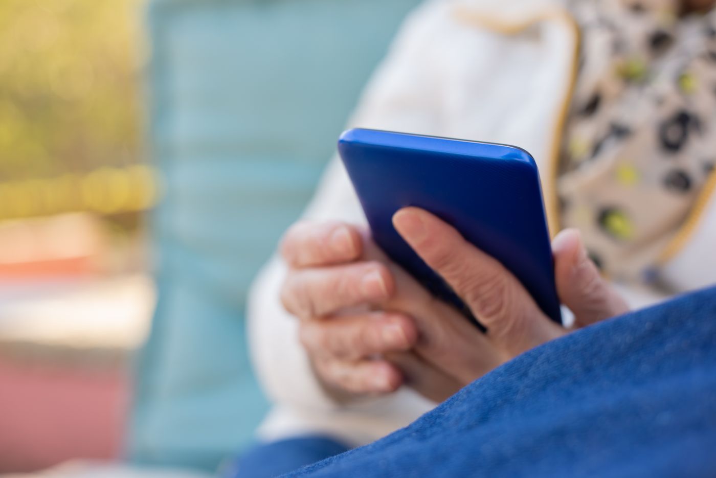 Hands holding a blue smartphone by its edges outdoors in warm natural light