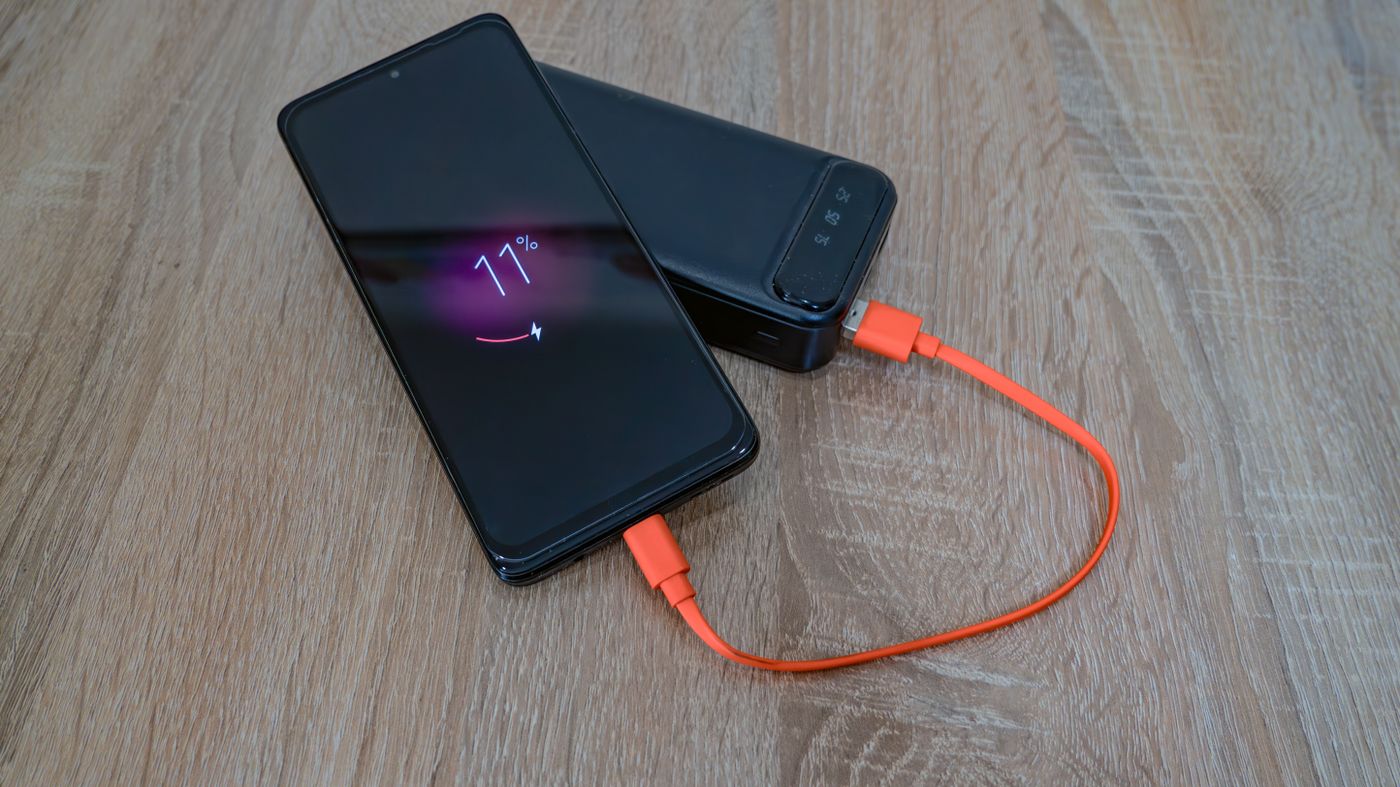 Android phone charging at eleven percent, orange USB-C cable running to a power bank