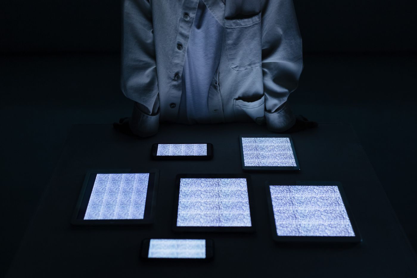 Phones and tablets on a dark table, all screens filled with static, person standing behind
