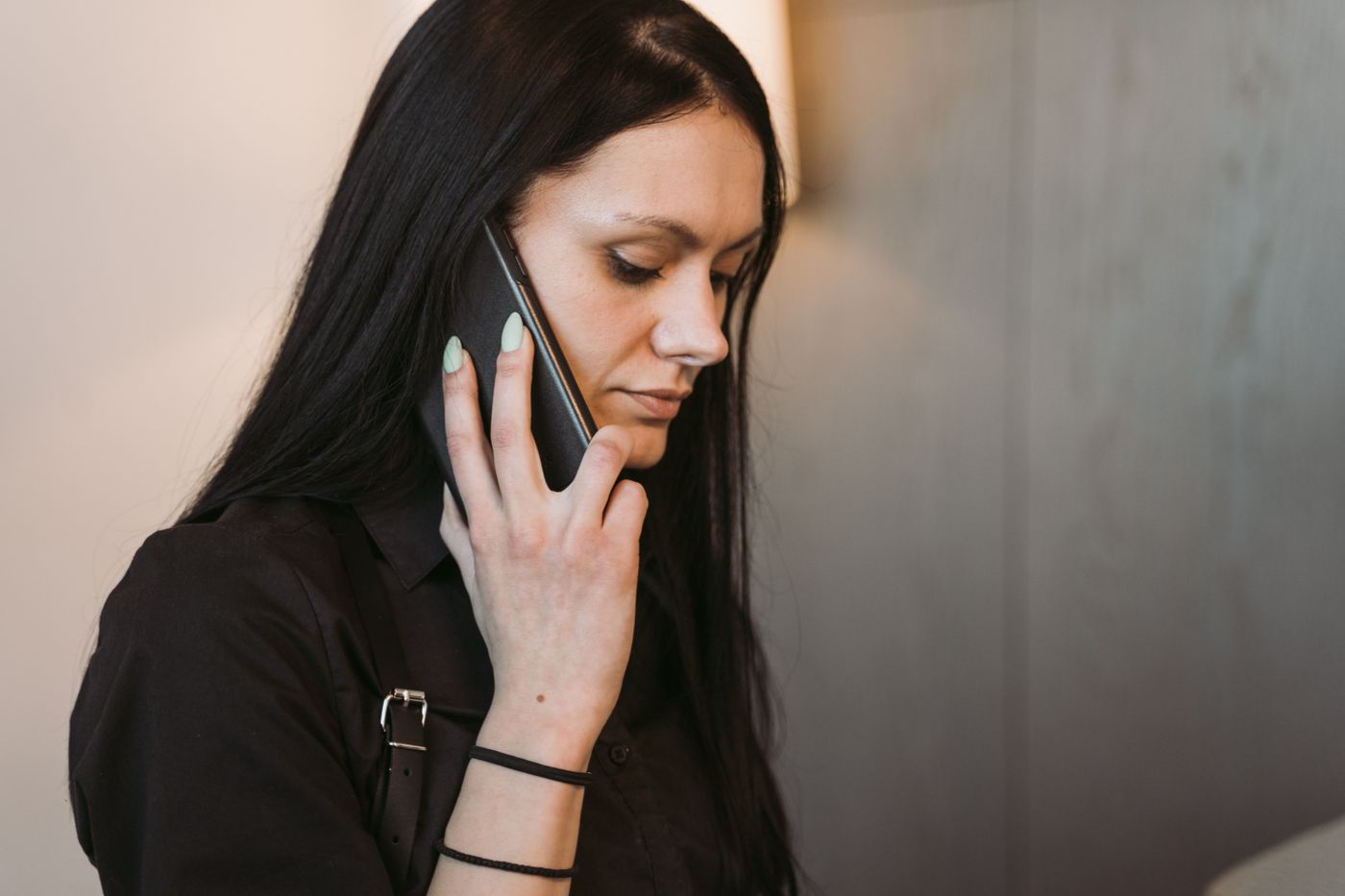 Woman holding a black smartphone to her ear during a call, head lowered, listening closely