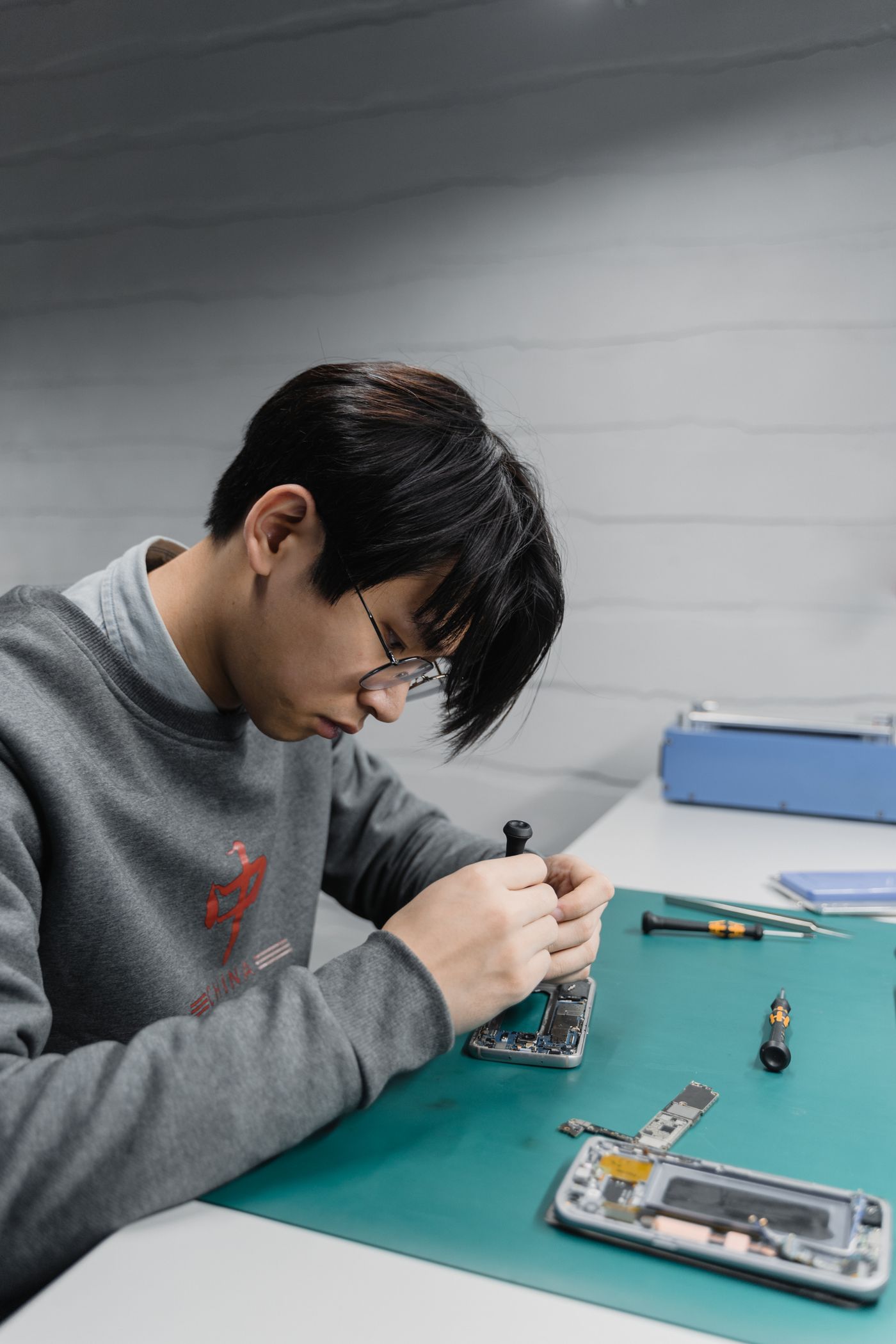 Technician at a repair bench beside an opened smartphone showing its battery and removed motherboard