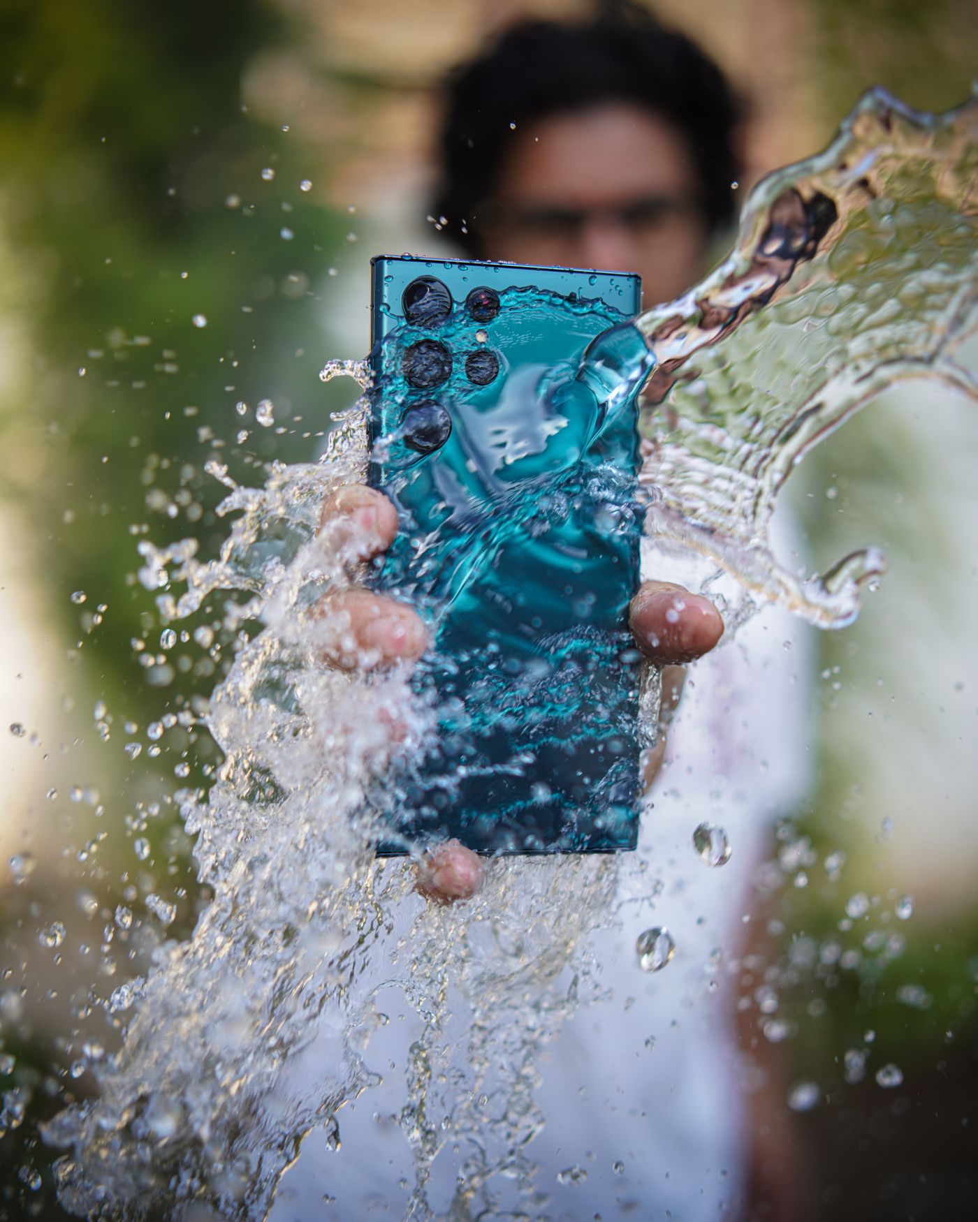 Water splashing across the multi-lens back of a smartphone gripped in a wet hand